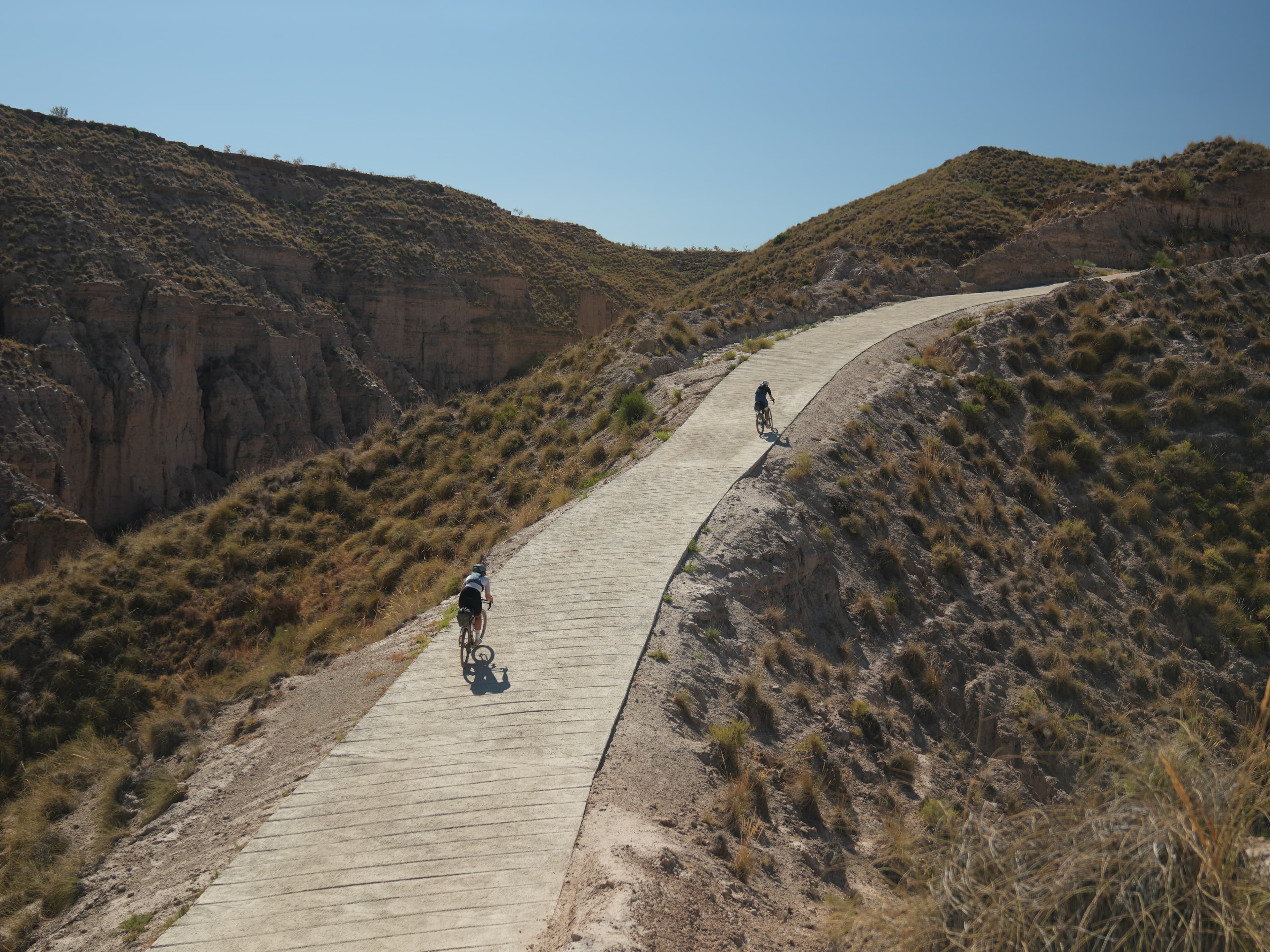 Two cyclists climbing a winding road through dramatic desert terrain
